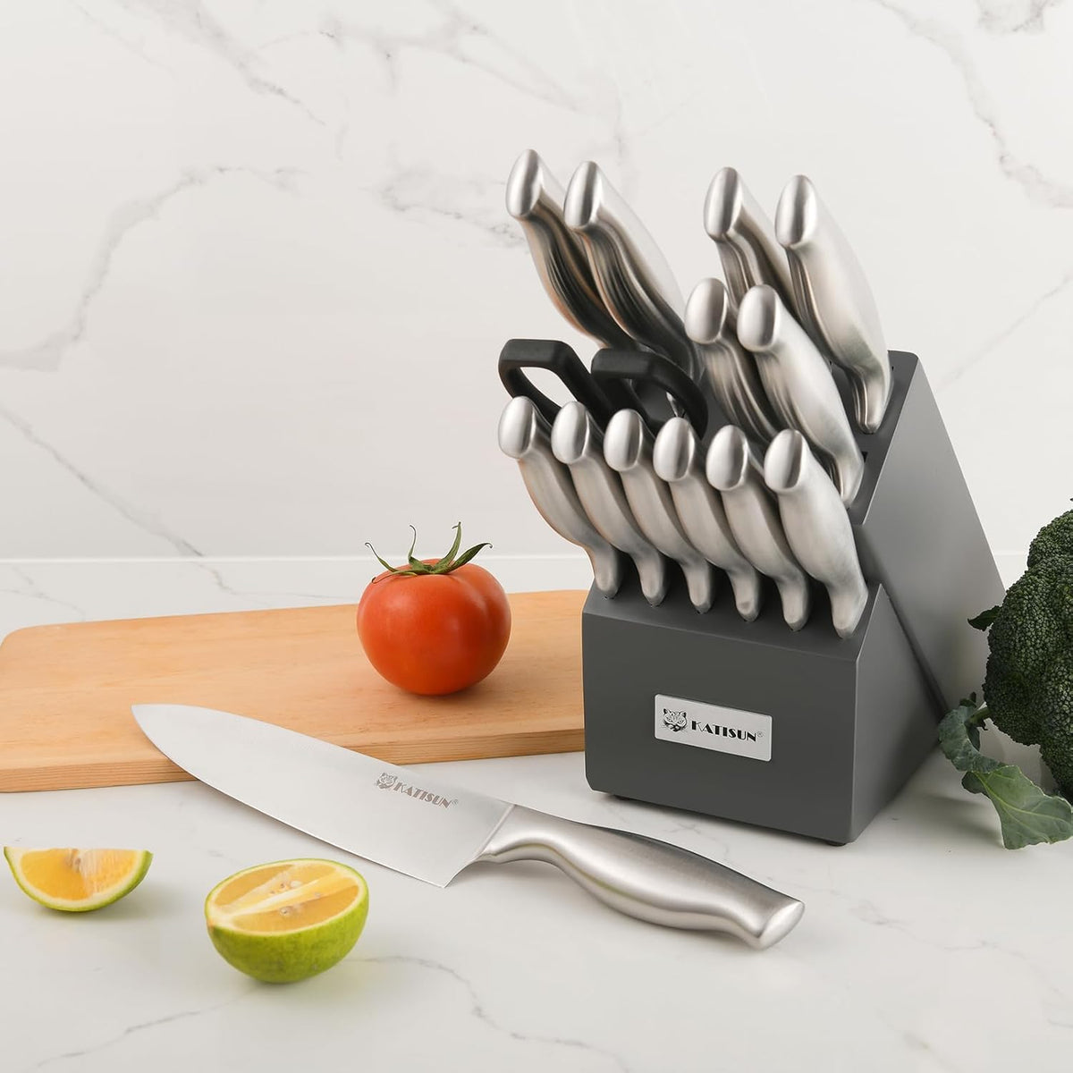 Set of knives in a block with a cutting board, tomato, lime, and broccoli on a white surface.