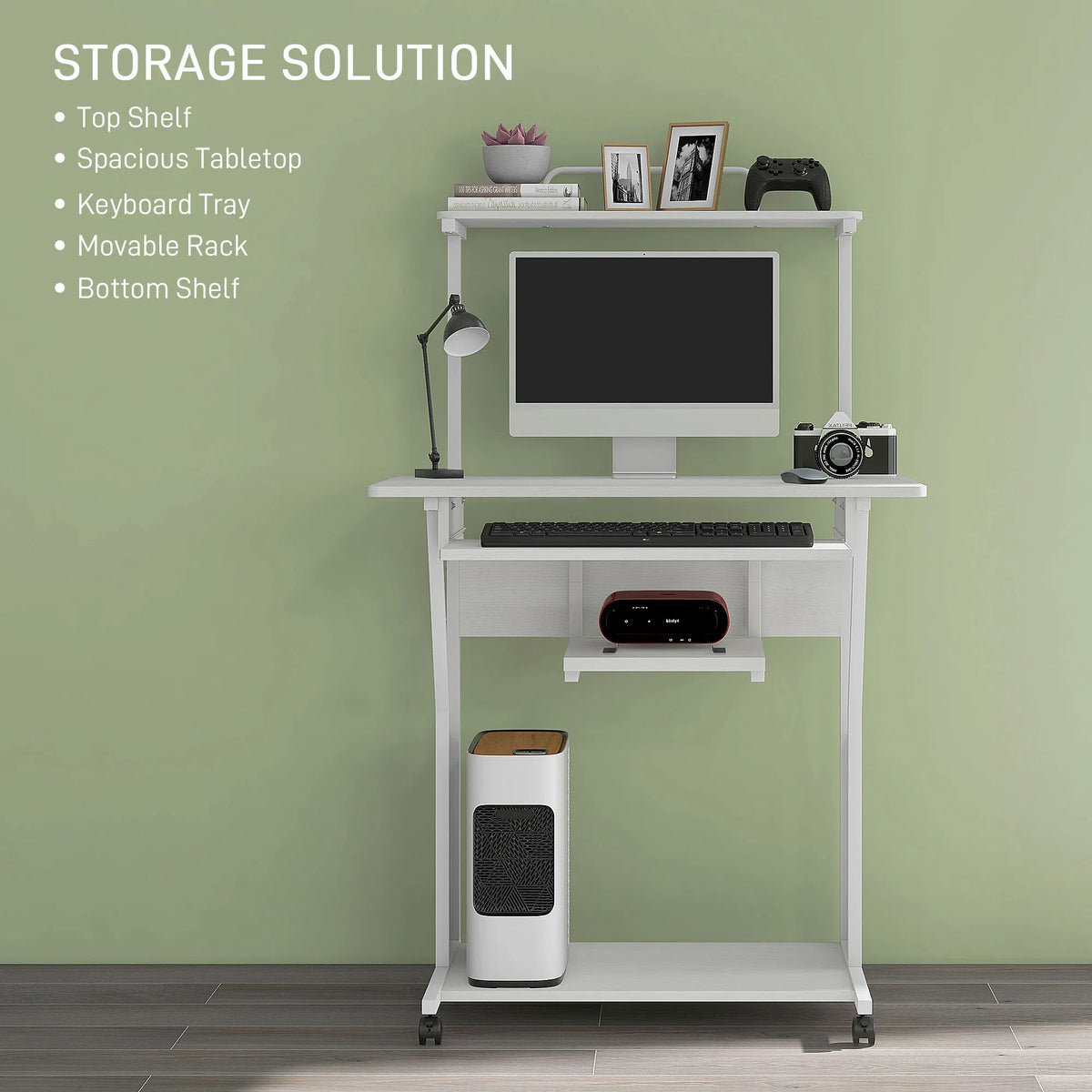 A white rolling computer desk with shelves, shown against a sage green wall. The desk includes a top shelf, spacious tabletop, keyboard tray, movable rack, and bottom shelf, styled with a computer monitor, lamp, camera, game controller, and other accessories.