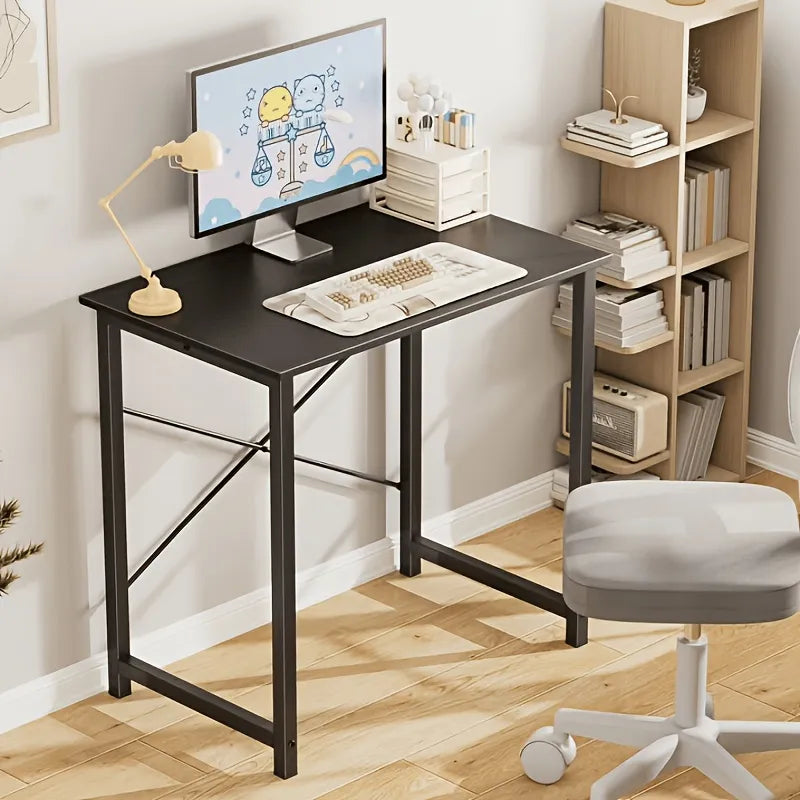 A black metal desk with a computer monitor, lamp, keyboard, and books, shown in a styled home office setting with a wooden floor, white stool, and shelving unit.